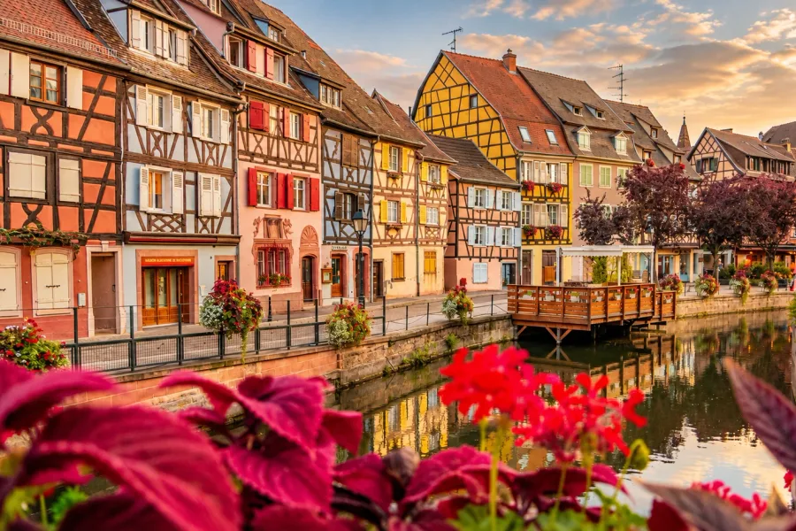 Colorful half-timbered houses along the Lauch canal in Colmar’s Little Venice district, Alsace, with flowers and reflections in the water.