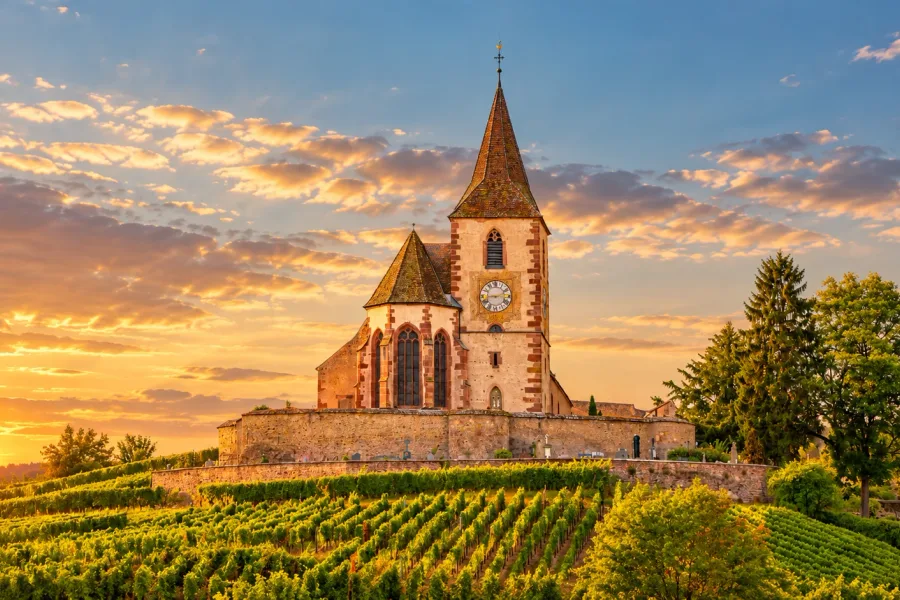 The fortified Saint-Jacques-le-Majeur Church in Hunawihr, surrounded by Alsatian vineyards beneath a cloudy sky.