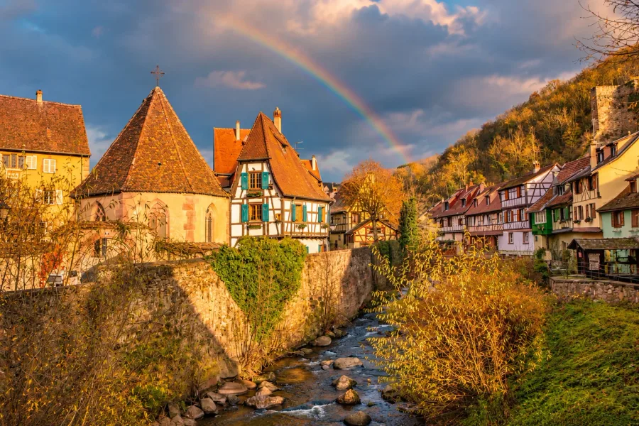Traditional half-timbered houses with turquoise shutters, red-tiled roofs and colorful flowers in Kaysersberg, Alsace.