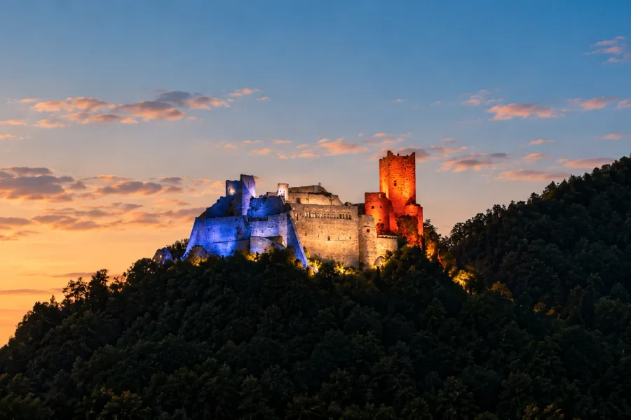 Saint-Ulrich Castle illuminated in blue, white and red above Ribeauvillé, Alsace, at dusk.